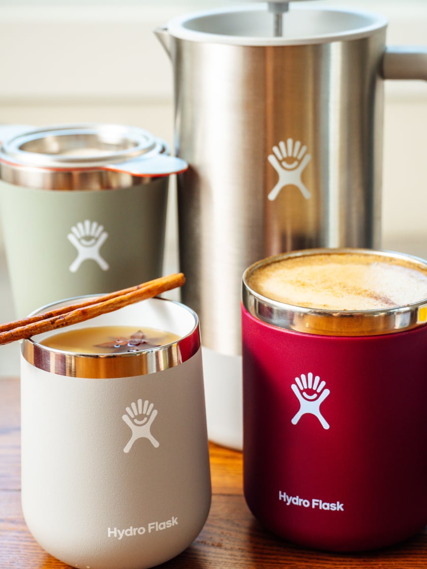 Trois délicieuses boissons d'automne sur un comptoir de cuisine en bois : un pumpkin spice latte dans une tasse couleur Berry, un cidre chaud à l'érable et au gingembre dans un tumbler à vin gris et agrémenté d'un bâton de cannelle, et un thé London fog dans un gobelet couleur Agave en acier inoxydable