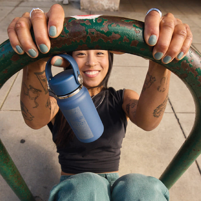 Girl swinging on a concrete bike rack holding a Hydro Flask Micro Hydro with a custom company engraving