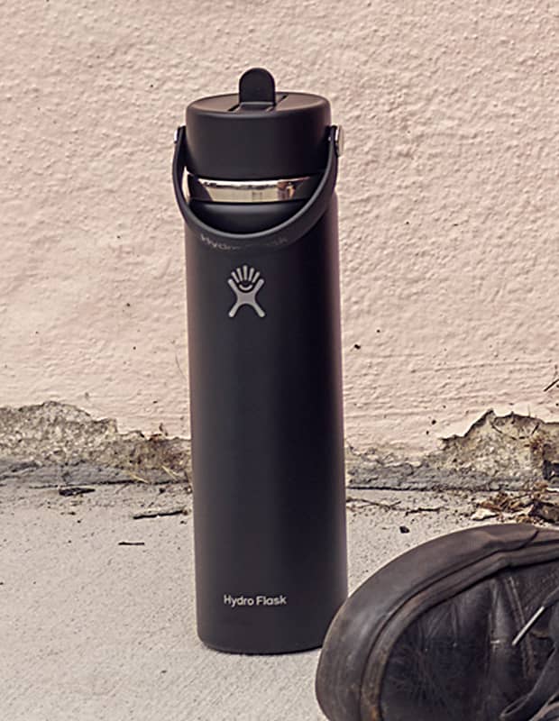 Black Hydro Flask straw bottle sitting outside on the curb next to a skateboard
