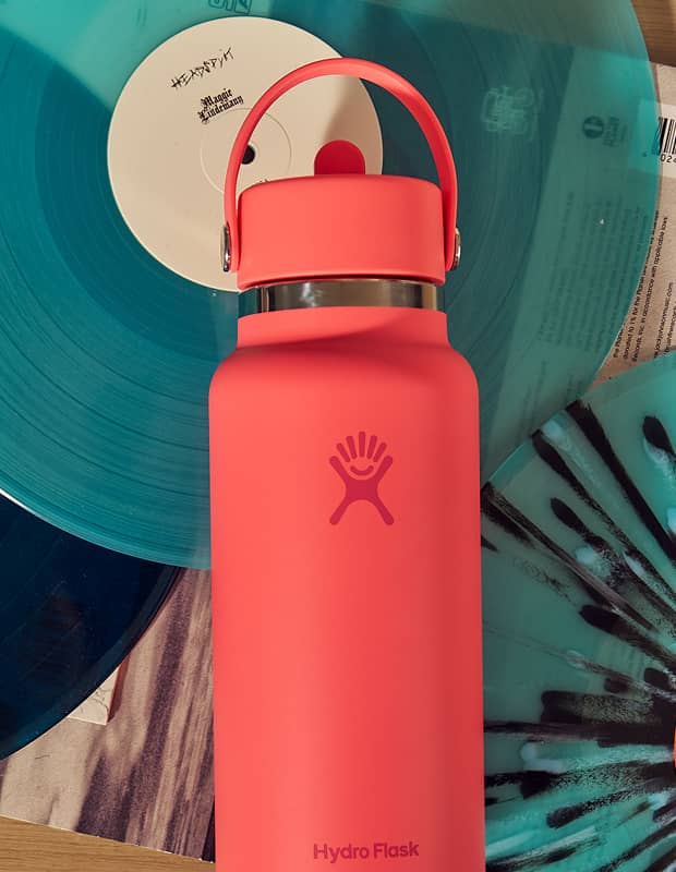 A Popstar Pink Hydro Flask straw bottle sitting on top of records