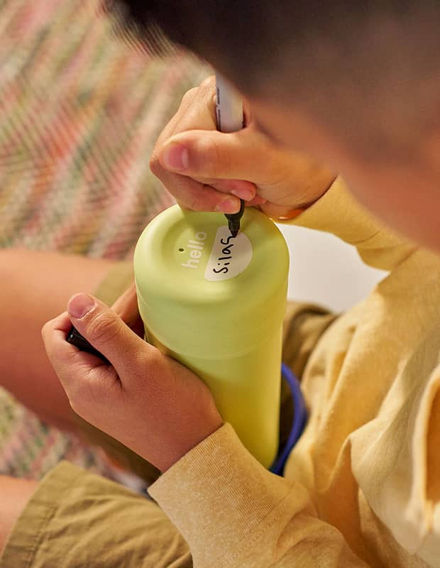 Child writing his name on the name tag on the underside of a Hydro Flask Kids Bottle