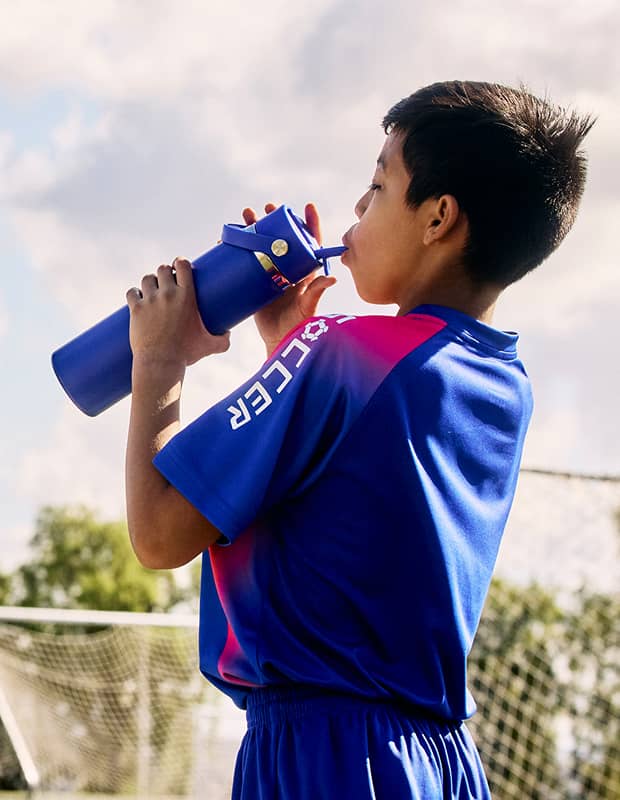 A middle school aged boy in a soccer uniform drinking from a 24 oz Hydro Flask bottle